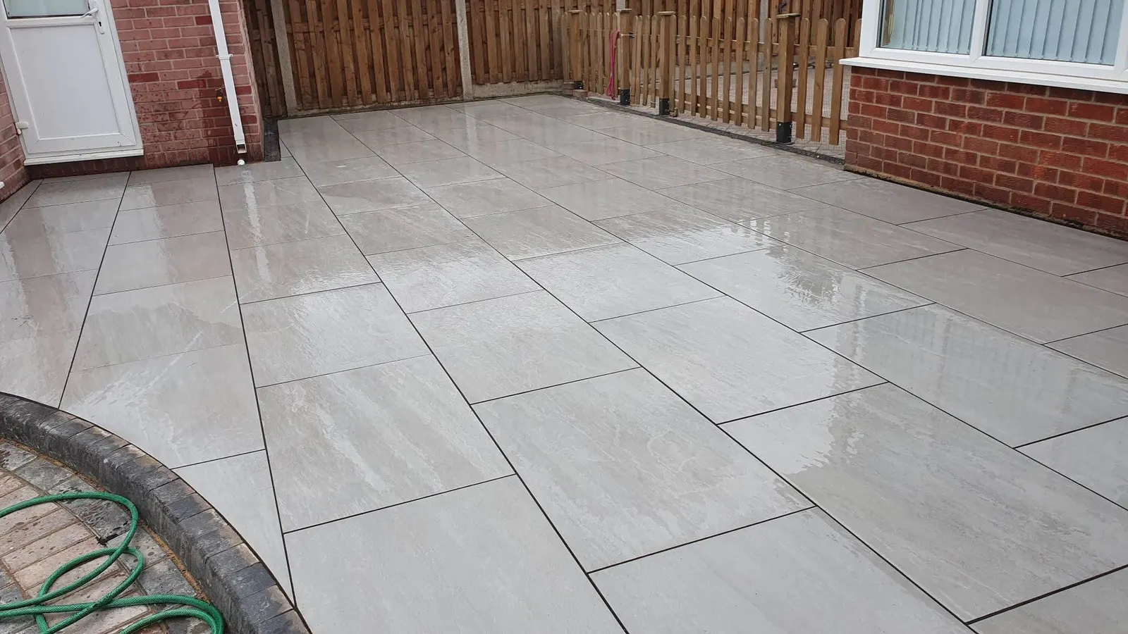 Light porcelain patio meeting a curved brick edge, wet after rain