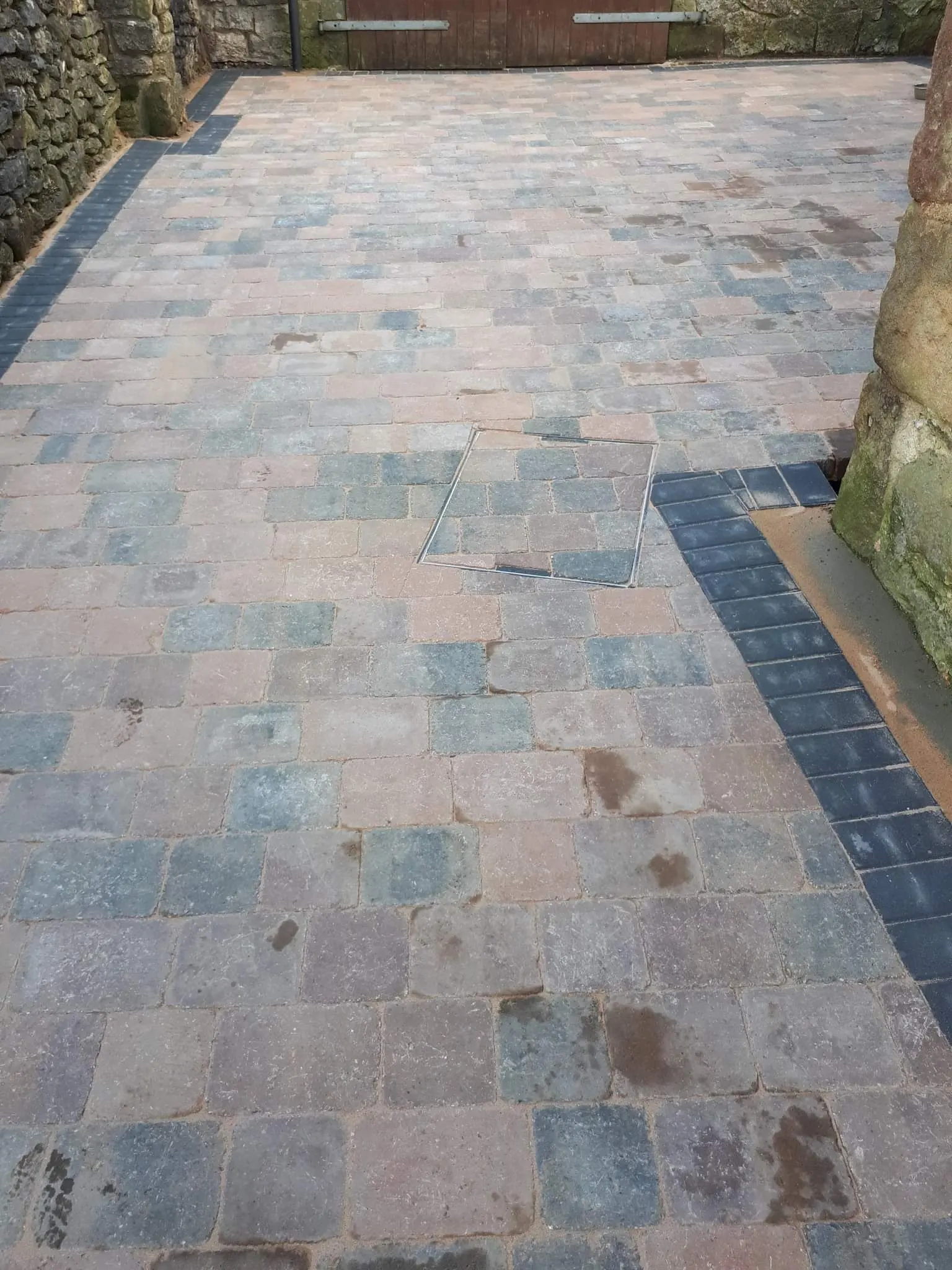 Multicolour block paving driveway with a charcoal border beside a stone wall
