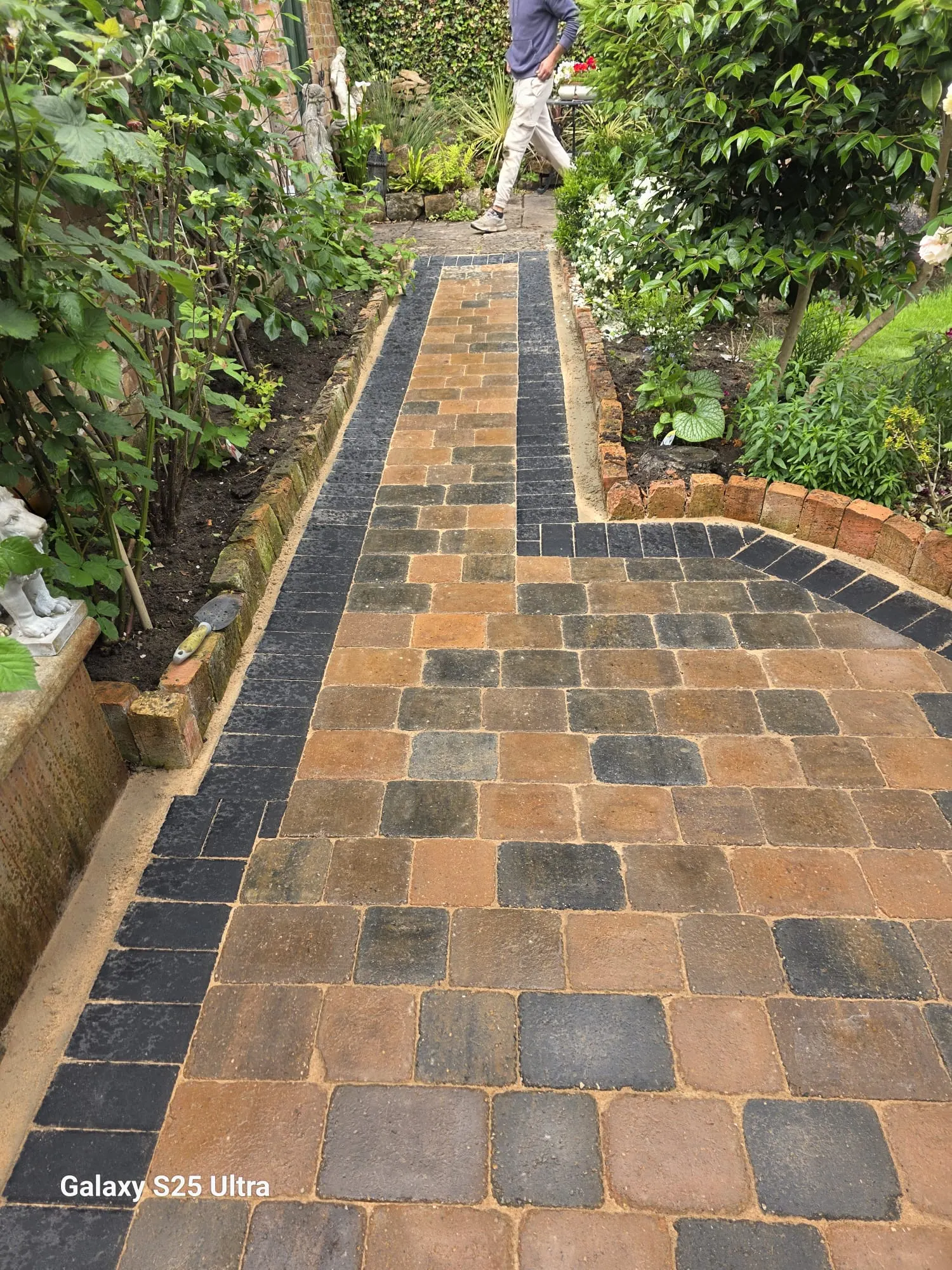Multicolour block paving garden path with a charcoal border beside planting