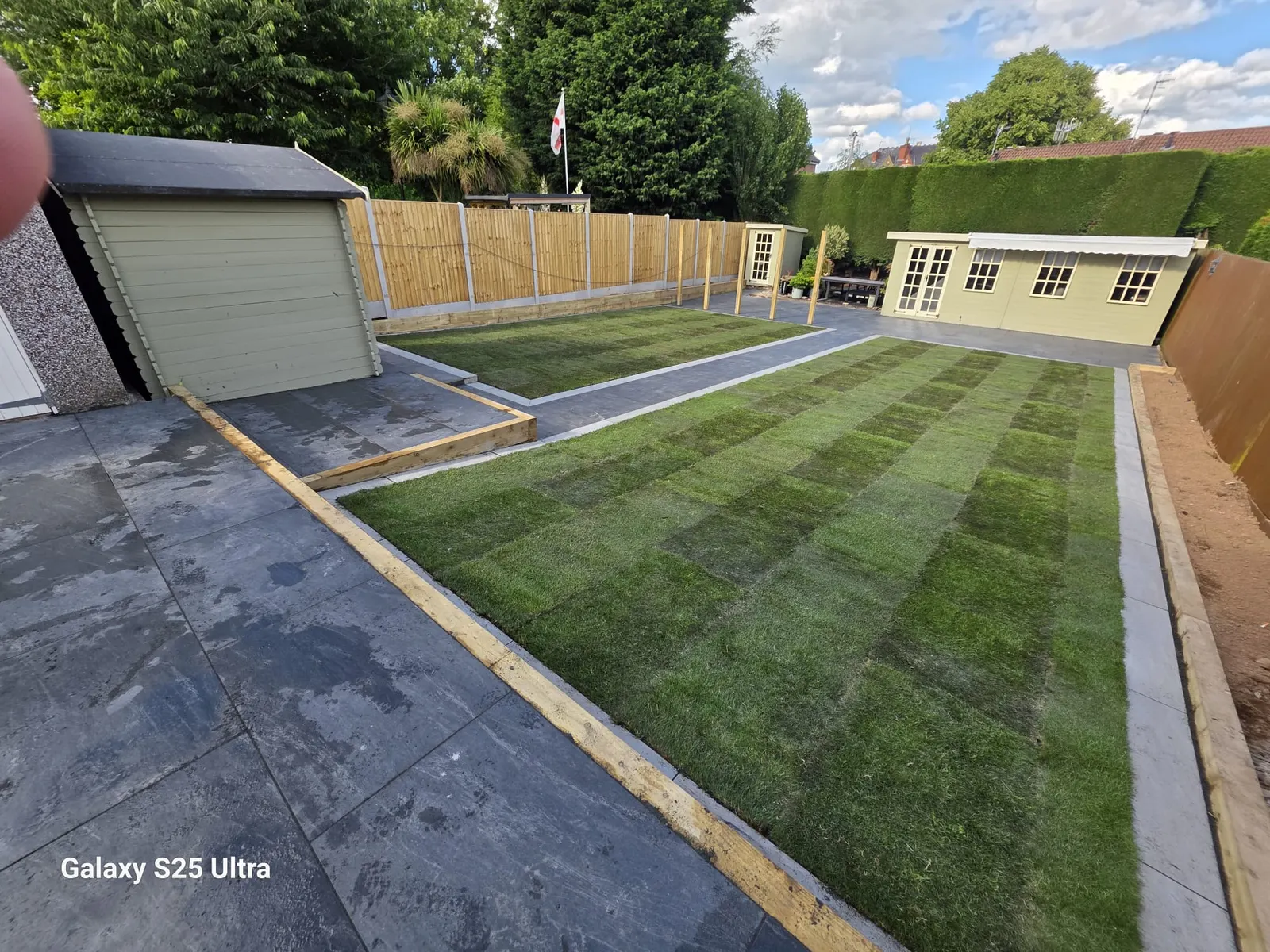 New turf lawn beside a grey patio and a shed