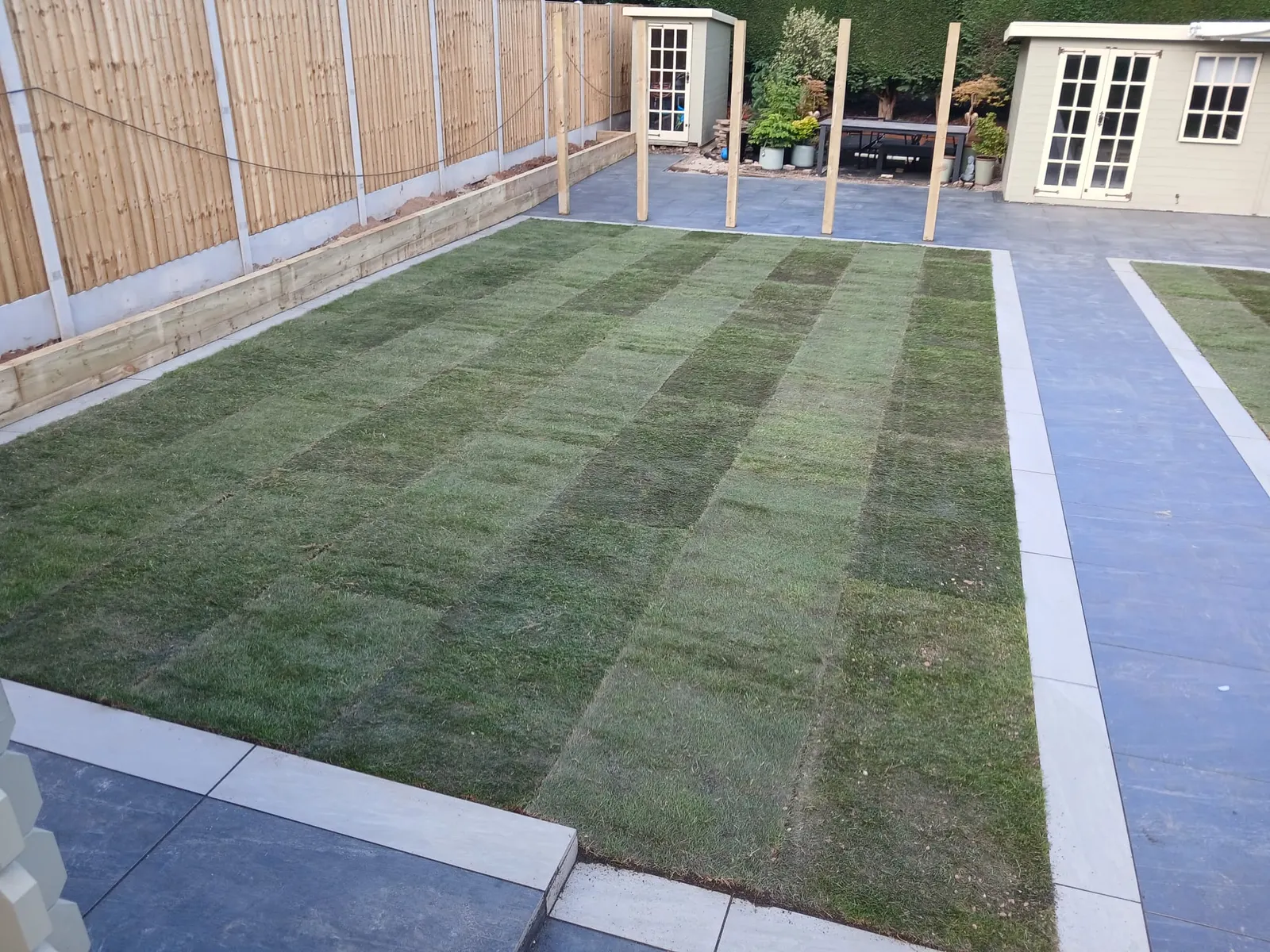 New striped turf lawn beside a grey porcelain path and a summer house