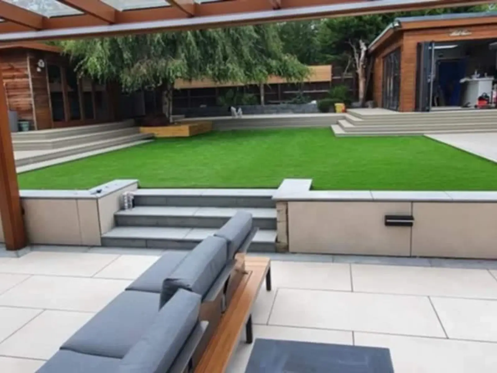 Porcelain patio with steps up to artificial grass and a garden room