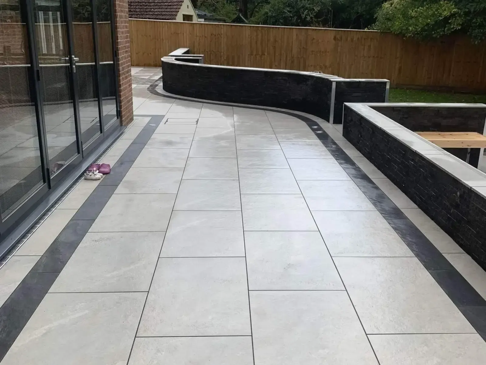 Porcelain patio curving past black raised planters and bifold doors