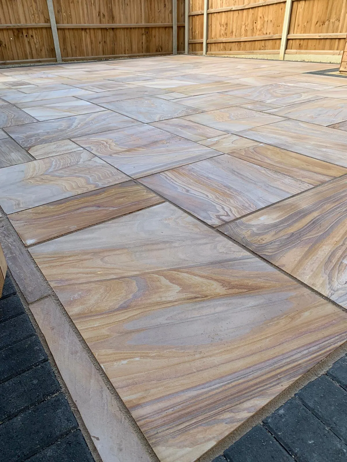 Rainbow sandstone patio edged with charcoal block paving