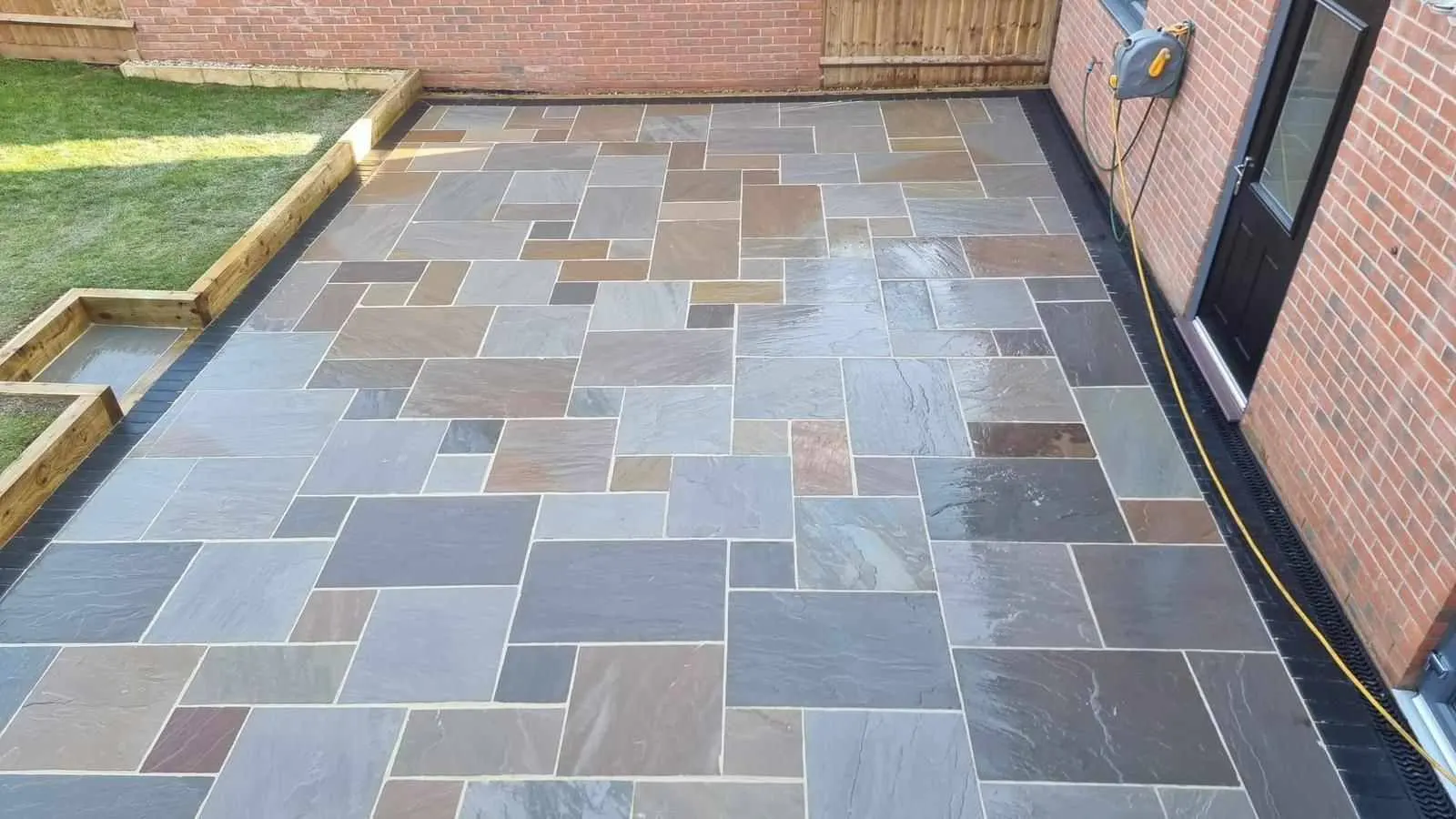 Rainbow sandstone patio with sleeper raised beds and a lawn