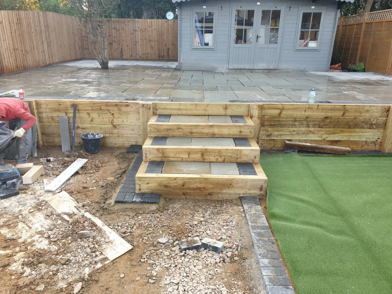 Raised sandstone patio with sleeper steps down to artificial grass