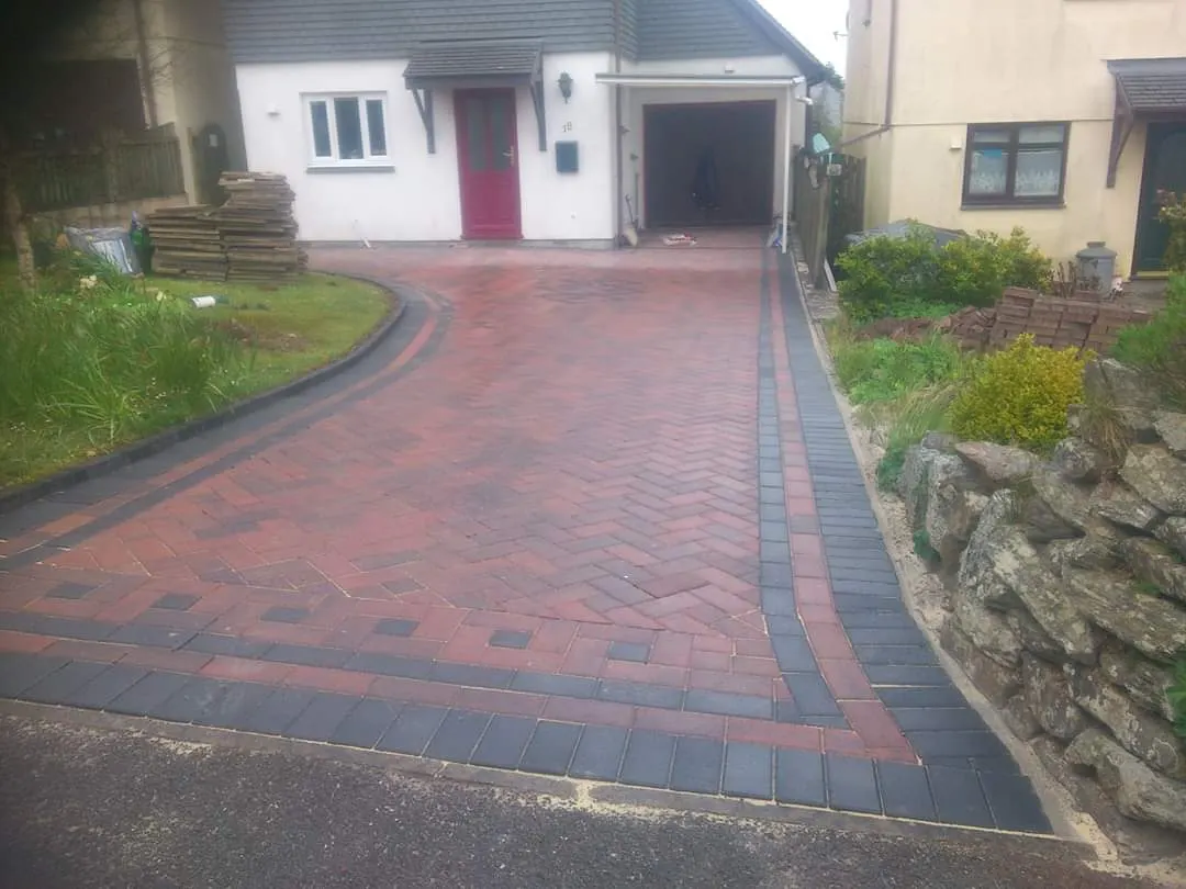 Red block paving driveway with charcoal bands beside a rockery