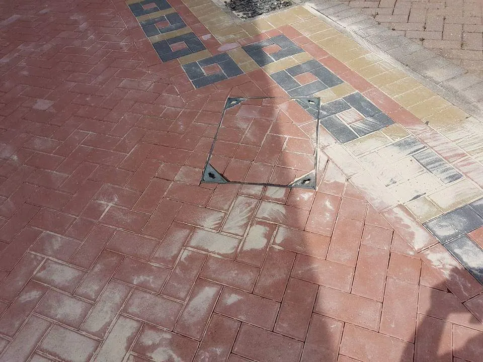 Red block paving with a patterned buff and charcoal border and a recessed cover