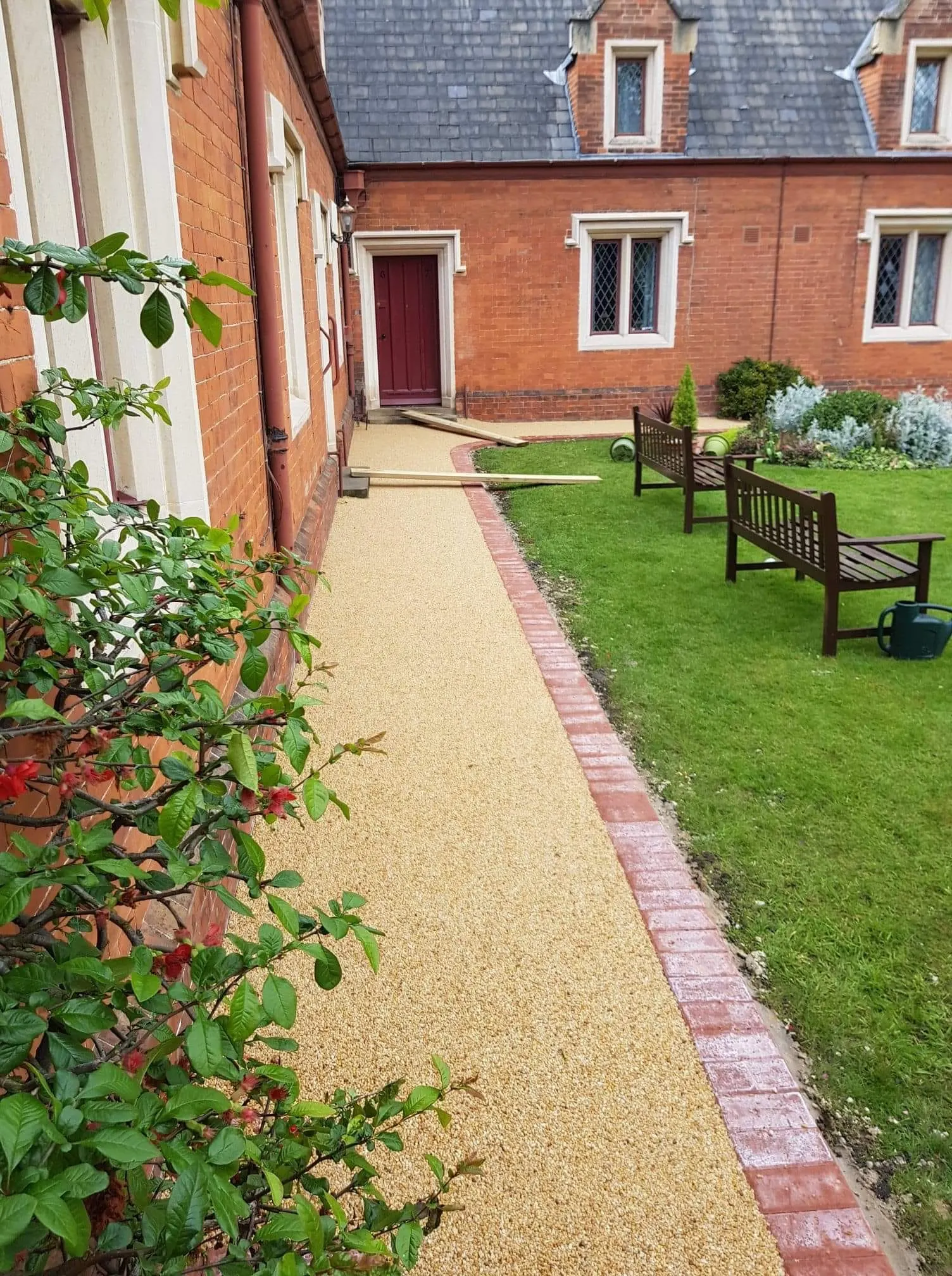 Resin bound path with red block paving edging beside a courtyard lawn with benches