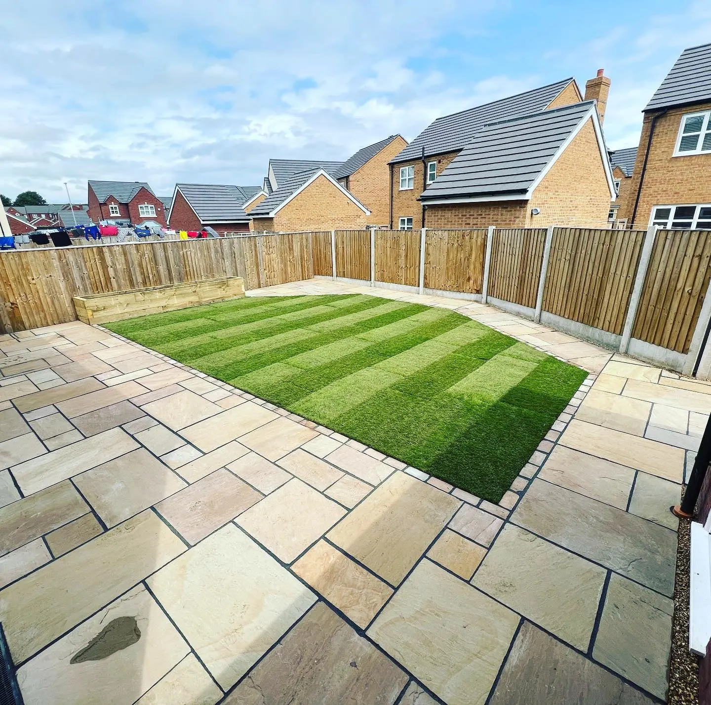 Sandstone patio round a striped lawn in a new-build garden