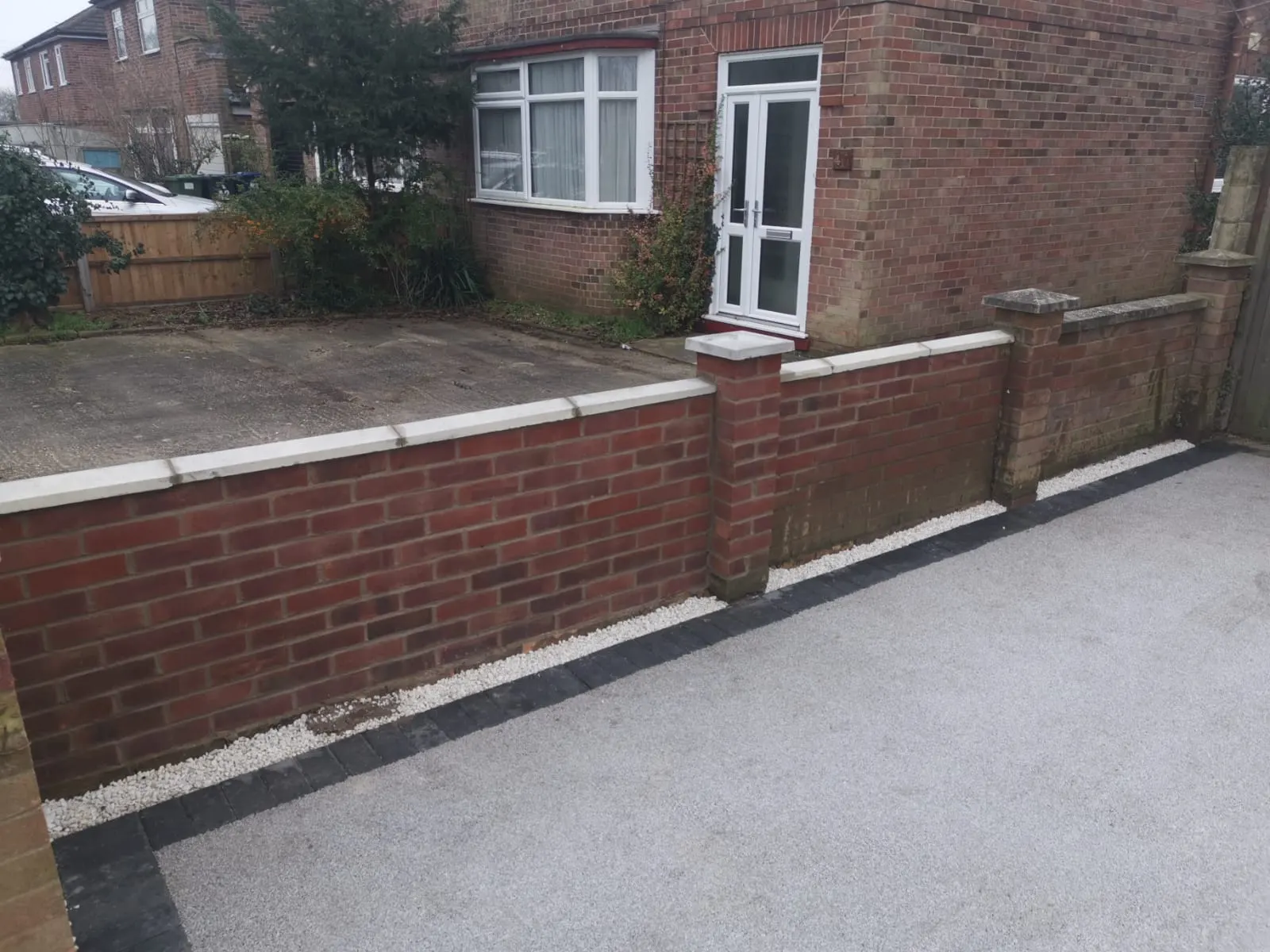 Silver resin bound driveway with a charcoal block border below a brick wall