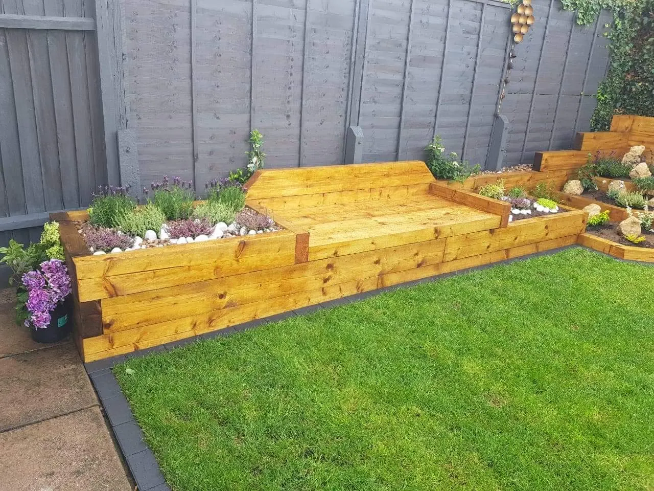 Sleeper raised beds and a bench planted with flowers beside a lawn
