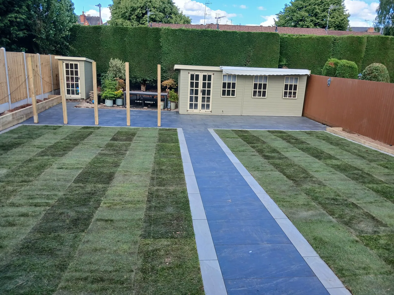Striped new turf lawns either side of a porcelain path to a garden room