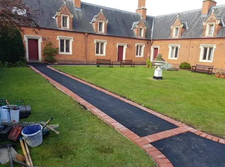Tarmac path with red brick edging being laid across a courtyard lawn