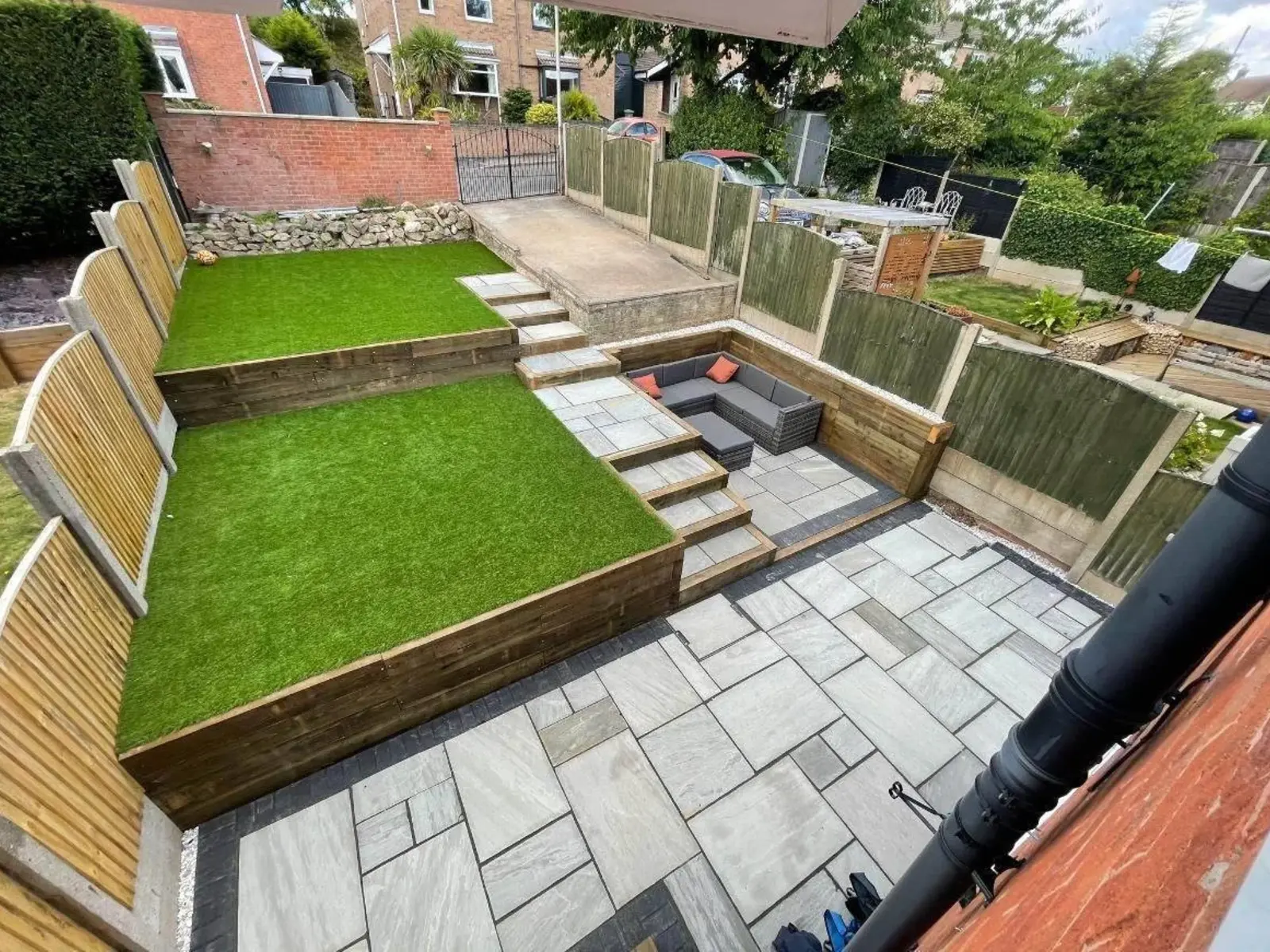 Tiered garden with artificial grass on sleeper terraces and a grey patio