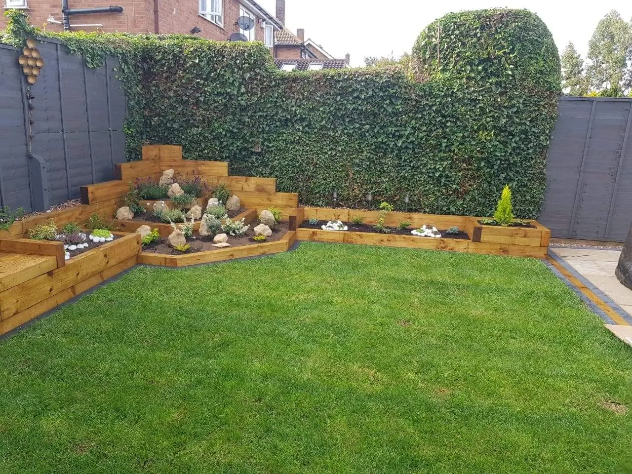 Tiered sleeper planters around a lawn in a fenced garden